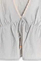 Blusa corta color celeste con textura arrugada, escote en V con puntilla, lazo ajustable en el frente y mangas 3/4 abullonadas con bordados florales a contraste.