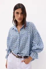 Camisa celeste con estampado de pequeñas flores blancas, cuello clásico, cierre con botones, mangas largas abullonadas con puños elásticos y corte holgado.