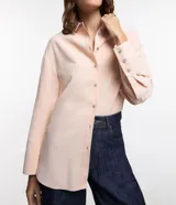 Camisa color rosa pálido, de corte amplio y alargado, confeccionada en viscosa. Tiene cuello camisero, abotonadura frontal y mangas largas con puños abotonados.