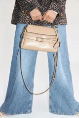 Cartera bandolera color visón, con correa ajustable y asa de mano. Presenta solapa con cierre magnético y trabilla decorativa con hebilla metálica.