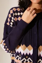 Cardigan azul marino de punto con cuello redondo y cierre frontal con botones. Presenta diseño con motivos geométricos en tonos beige, blanco y rosa, y un dibujo de un cupido en el pecho.