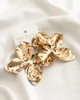 Par de aros colgantes con forma de flor de cinco pétalos, color dorado con textura irregular.