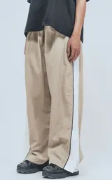 Pantalón deportivo beige de nylon con cintura elástica ajustable con cordón, corte amplio y aberturas laterales con broches.