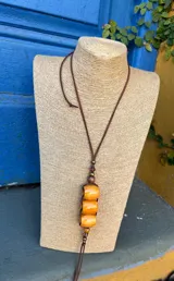 Collar largo con cordón de cuero marrón y dije colgante con cuentas cilíndricas color ámbar y detalles de cuentas de madera y bronce.