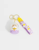 Llavero con dije de gatito dentro de una burbuja con base lila y correa de silicona lila con diseño de letras y dibujos en amarillo y blanco.