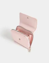 Billetera pequeña de cuerina color negro con cierre de cremallera y broche. Presenta un moño metálico en el frente.
