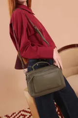 Bandolera color marrón con asa superior y correa larga ajustable. Tiene dos bolsillos frontales, uno de ellos con cierre cruzado.