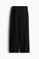 Pantalón negro de corte ancho y tiro alto, con elástico en la parte posterior de la cintura, cierre oculto con corchete en un lado, bolsillos laterales discretos y pliegues adelante y atrás.