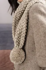 Bufanda tejida a mano en punto arroz color beige, con pompones en los extremos.