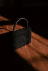 Cartera de mano negra con textura brillante y asa corta rígida.
