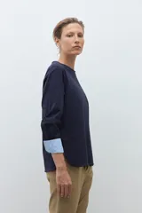 Remera de manga larga color azul marino con cuello redondo. Los puños de las mangas son doblados y revelan un forro de tela a rayas finas blancas y celestes.