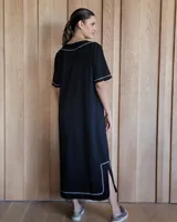 Vestido midi negro con cuello redondo y mangas cortas. Presenta dos bolsillos cuadrados en el pecho y ribetes blancos en cuello, mangas, bolsillos y ruedo.