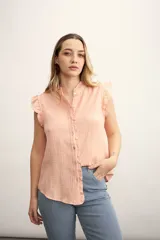 Camisa color salmón con textura arrugada, cuello mao con volados, mangas cortas con volados y cierre frontal con botones.