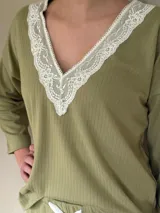 Pijama verde con textura acanalada, compuesto por un top de mangas largas con escote en V con puntilla blanca y un pantalón recto con lazo blanco en la cintura.