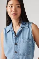 Mono de jean celeste claro, sin mangas, con cuello camisero, cierre frontal con botones y bolsillos laterales.
