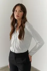 Remera blanca de mangas largas con escote en V y costuras decorativas en negro.