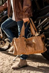 Bolso de cuero hecho a mano en color tostado, con diseño amplio y funcional. Presenta cierre superior, bolsillo frontal con cremallera, asas de mano reforzadas y una correa larga ajustable y desmontable.