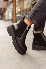 Botines negros de cuero con caña baja, puntera redondeada y cierre frontal con cremallera. Presentan paneles laterales de gamuza y suela track con plataforma.