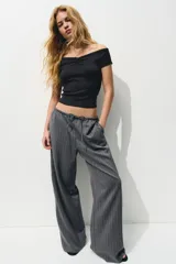 Pantalón gris oscuro a rayas verticales finas, de corte holgado, con elástico y cordón ajustable en la cintura, bolsillos laterales y bolsillos decorativos en la parte trasera. Confeccionado en sarga.