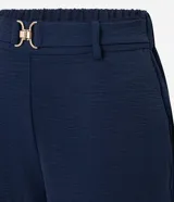 Pantalón zanahoria de cintura alta, confeccionado en tejido airflow color azul marino, con trabillas, cintura elástica y hebillas metalizadas.