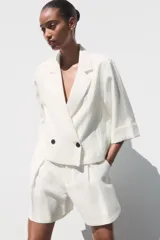 Blazer blanca de cuello solapa y manga corta con vuelta. Bolsillos delanteros de vivo y cierre frontal cruzado con botones.