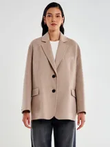 Chaqueta de lana color beige, de corte recto y levemente oversize, con solapa clásica y cierre de dos botones negros. Posee bolsillos con tapa a la altura de la cadera y un bolsillo de ojal en el pecho.