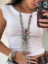 Collar largo plateado con cadena de eslabones y colgantes de piedras de colores en tonos rosa, blanco, rojo y turquesa. Incluye dijes plateados con forma de monedas y borlas de cadenas. Estilo boho.