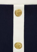 Minifalda azul marino de tejido de punto con ribete blanco en cintura y bolsillos. Presenta dos bolsillos delanteros con solapa y botones dorados decorativos.