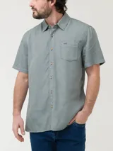 Camisa de manga corta color beige, con cuello clásico, cierre frontal con botones y bolsillo en el pecho izquierdo.