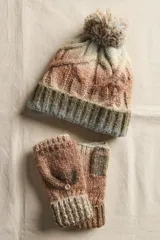 Set de invierno compuesto por un gorro de punto con pompón y guantes mitones con solapa rebatible. Ambas piezas están confeccionadas en un tejido de punto grueso con diseño de ochos y puños acanalados.