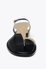 Sandalia plana color beige de cuero gamuzado, con tira entre los dedos y pulsera con hebilla ajustable.