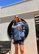 Camisa celeste de jean liviano con mangas largas abullonadas y puños elastizados. Presenta un bolsillo de cuero marrón en el pecho.