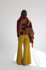 Ruana de lana con diseño abstracto en tonos beige, marrón y blanco. Presenta flecos en el borde inferior y capucha.