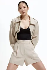 Short color beige de tiro alto con pliegues delanteros, bolsillos al bies y cierre frontal con botón y corchete ocultos.