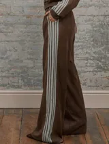 Conjunto deportivo marrón de dos piezas: campera con cremallera, cuello alto, mangas largas con puño y detalles de rayas blancas en mangas y laterales del pantalón. Pantalón recto de cintura alta con cordón ajustable.