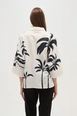 Camisa blanca con estampado de palmeras en color azul marino, de corte holgado, con cuello camisero, cierre frontal con botones y mangas 3/4 con puños anchos.