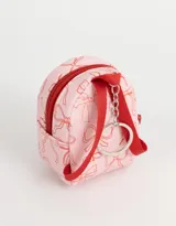 Llavero con forma de mochila pequeña color rosa claro con estampado de moños rojos y cierre con cremallera roja.