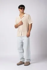 Camisa negra tejida de manga corta, con calado aireado, cuello tipo bowling y botones al tono. Diseño de corte relajado.