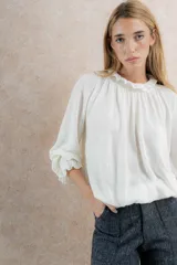 Blusa color crema de tela tejida 100% lana, con cuello fruncido y mangas largas con puños elásticos.