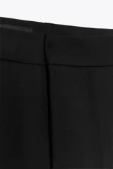 Pantalón negro de tiro medio con trabillas en la cintura, pernera recta y corte cropped. Cierre frontal con cremallera y ganchos metálicos.