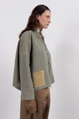 Camisa amplia de lino en tono verde desgastado, con textura visual y caída liviana. Destaca por su parche tejido a mano en contraste, que aporta un detalle artesanal y único.