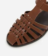 Sandalias planas de cuero marrón con tiras entretejidas, hebilla dorada y suela negra.