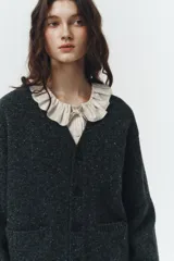 Cardigan de punto gris oscuro jaspeado, con cuello en V, cierre frontal de botones y dos bolsillos frontales tipo parche. Corte relajado y holgado.