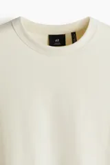 Remera color crema de punto pesado con cuello redondo ribeteado, hombros caídos y bajo recto. Corte holgado confeccionada con tejido funcional Coolmax, una fibra de poliéster de secado rápido que elimina la humedad y regula la temperatura corporal.