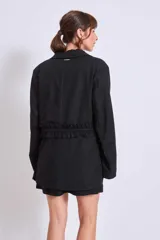 Blazer marrón con solapas de muesca, cierre frontal con lazo y mangas largas. Presenta volados a lo largo de las costuras laterales del pantalón a juego.