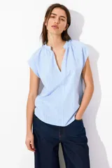Blusa celeste a rayas verticales blancas, de corte holgado, manga corta y cuello mao con escote en V.