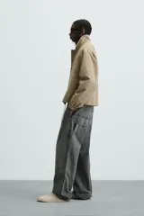 Cazadora color arena de corte relaxed fit, confeccionada en tejido de algodón. Cuenta con cuello solapa, manga larga con bolsillo multifunción, bolsillos frontales de plastrón, bolsillo interior, acabados con elástico y bajo ajustable con cordón. Cierre frontal con cremallera oculta por solapa con botones a presión.