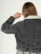 Campera de jean gris oscuro con cuello de piel sintética blanca, cierre frontal con cremallera, bolsillos laterales y puños con cremallera.