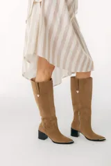 Bota bucanera de cuero color marrón, con caña alta, punta fina y taco cuadrado. Presenta detalle de costuras verticales en la caña y cierre lateral.