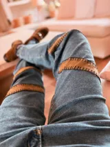 Pantalón de jean azul con corte holgado y apliques de gamuza marrón bordados a mano en los laterales.